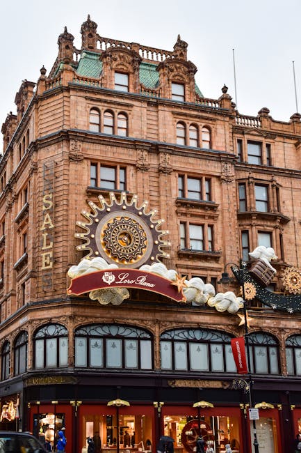 A bustling street scene in Knightsbridge near Harrods featuring historic multi-story buildings with ornate facades, large glass windows, and decorative architectural details. The street is lined with 